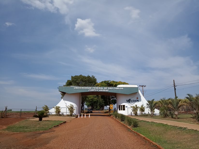 Entrada do campus da UFSCar de Araras. Pilares do pórtico de cor branca, pilar do lado direito há o logo da UFSCar. A parte superior do pórtico é de cor verde e com os dizeres escritos em branco